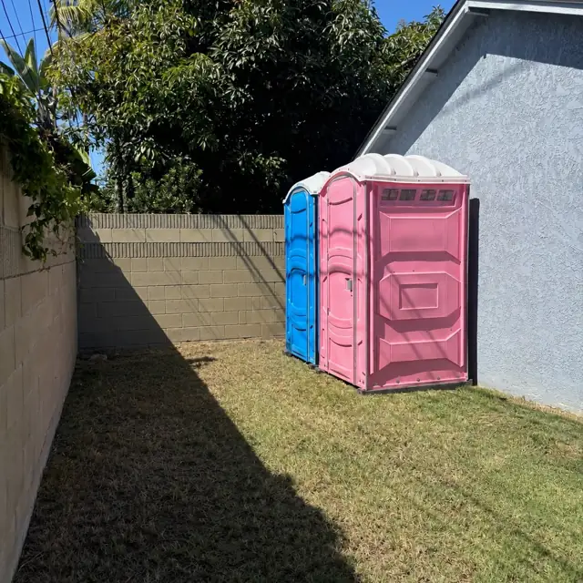 Two porta potties placed in a backyard along a wall