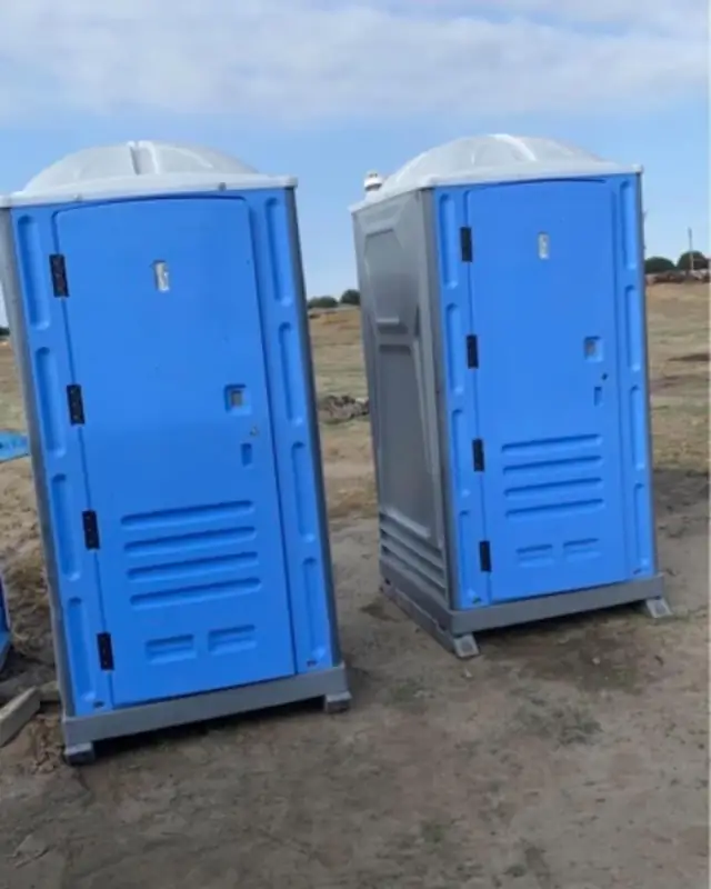 Two blue porta potties on a dirt job site